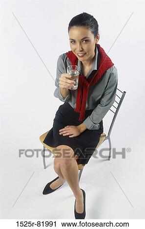 Portrait of young woman sitting on a chair holding a glass of water View Large Photo Image Stock Image - Portrait of young woman sitting on a chair holding a glass of water. Fotosearch