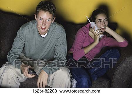 Teenage boy and a teenage girl sitting together on a couch watching television View Large Photo Image Stock Photo - Teenage boy and a teenage girl sitting together on a couch watching television. Fotosearch
