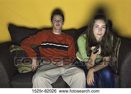 Teenage boy and a teenage girl sitting together on a couch watching television View Large Photo Image Stock Photograph - Teenage boy and a teenage girl sitting together on a couch watching television. Fotosearch