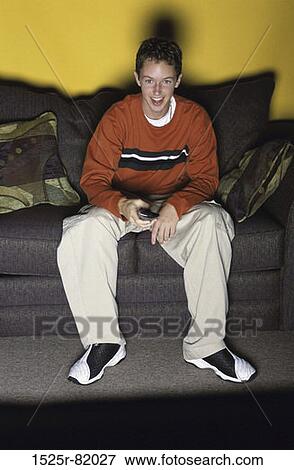 Stock Photo - Teenage boy sitting on a couch watching television. Fotosearch