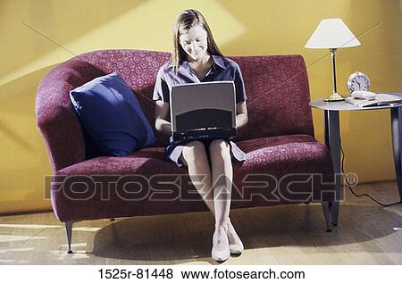 Young woman sitting on a couch using a laptop View Large Photo Image Stock Photo - Young woman sitting on a couch using a laptop. Fotosearch