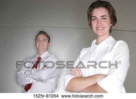Picture - Business man and business woman cross their arms and stand next to each other as they look at the camera. Fotosearch