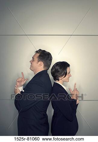 Stock Image - Business man and business woman stand back to back with their hands in the shape of guns. Fotosearch