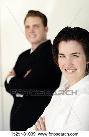 Stock Photo - Business man in black smiles as he stands behind woman dressed in white. Fotosearch
