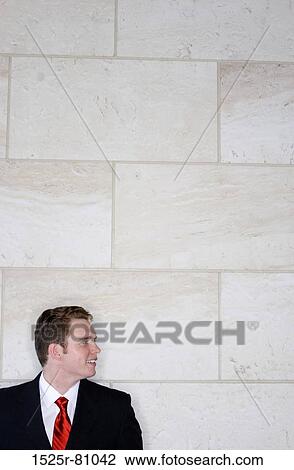 Stock Image - Business man in black suit and red tie against a brick wall. Fotosearch