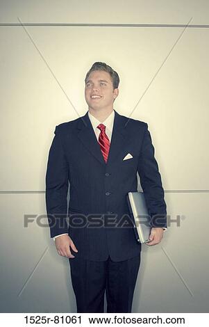 Business man in black suit and red tie stands as he holds laptop View Large Photo Image Stock Image - Business man in black suit and red tie stands as he holds laptop. Fotosearch