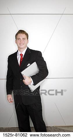 Business man in black suit and red tie standing and holding laptop View Large Photo Image Stock Image - Business man in black suit and red tie standing and holding laptop. Fotosearch