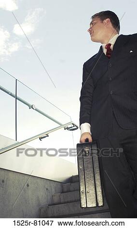 Business man in black suit and red tie smiles as he holds briefcase View Large Photo Image Stock Photo - Business man in black suit and red tie smiles as he holds briefcase. Fotosearch