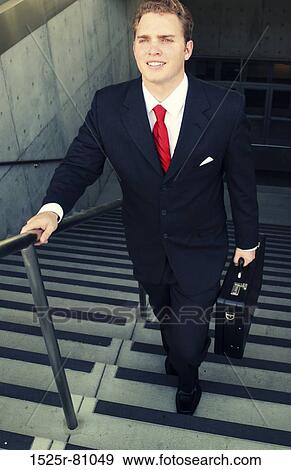 Business man in black suit and red tie smiles as he walks up the stairs View Large Photo Image Stock Photo - Business man in black suit and red tie smiles as he walks up the stairs. Fotosearch