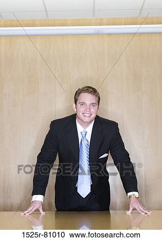 Business Man stands over the table with his hands on the table in the board room View Large Photo Image Stock Image - Business Man stands over the table with his hands on the table in the board room. Fotosearch