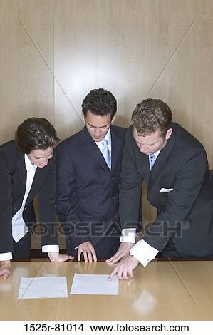 Business People in a board room pointing at a document on the table looking down View Large Photo Image Picture - Business People in a board room pointing at a document on the table looking down. Fotosearch