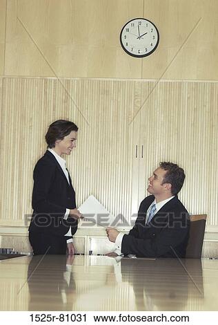 Business woman hands over papers to business man who is sitting at the head of the conference table View Large Photo Image Stock Image - Business woman hands over papers to business man who is sitting at the head of the conference table. Fotosearch
