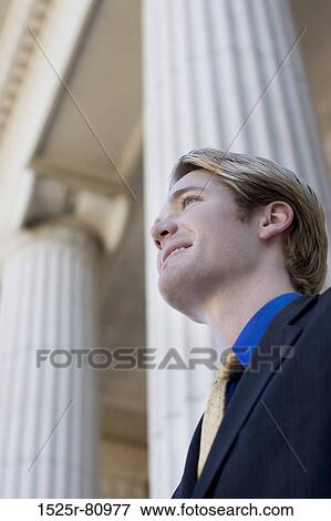 Businessman looks ahead and smiles as he stands in front of columns View Large Photo Image Stock Photo - Businessman looks ahead and smiles as he stands in front of columns. Fotosearch