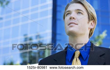 Businessman looks ahead as he stands in front of a blue business building View Large Photo Image Stock Image - Businessman looks ahead as he stands in front of a blue business building. Fotosearch