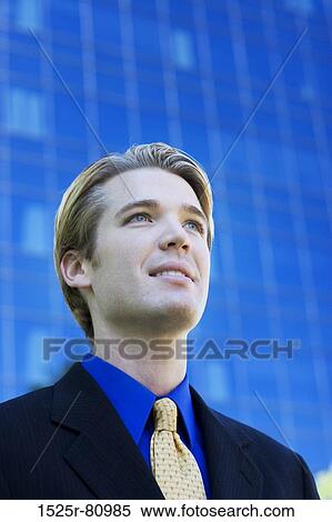 Businessman smiles and stands in front of a blue business building View Large Photo Image Stock Photography - Businessman smiles and stands in front of a blue business building. Fotosearch
