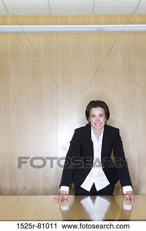 Stock Image - BusinessWoman standing with her hands on the table and a smile on her face in the board room. Fotosearch