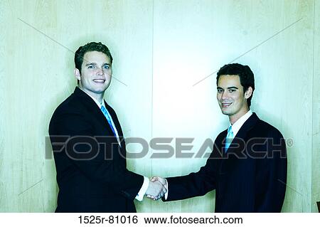 Two business men smiling and giving a handshake in an office room View Large Photo Image Stock Photograph - Two business men smiling and giving a handshake in an office room. Fotosearch