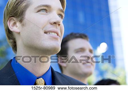 Two businessmen smiling as they stand together in front of a business building View Large Photo Image Stock Photo - Two businessmen smiling as they stand together in front of a business building. Fotosearch