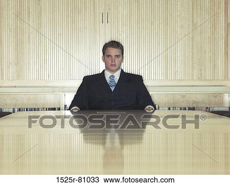 Younger business man sits down at the end of a wooden conference table View Large Photo Image Stock Image - Younger business man sits down at the end of a wooden conference table. Fotosearch