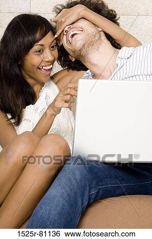 Close-up of a young couple sitting in front of a laptop and laughing View Large Photo Image Stock Photograph - Close-up of a young couple sitting in front of a laptop and laughing. Fotosearch