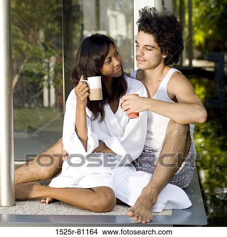 Close-up of a young couple sitting on the floor and holding cups of tea View Large Photo Image Picture - Close-up of a young couple sitting on the floor and holding cups of tea. Fotosearch