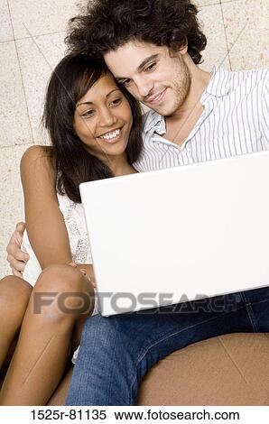 Close-up of a young couple sitting together and looking at a laptop View Large Photo Image Stock Photography - Close-up of a young couple sitting together and looking at a laptop. Fotosearch
