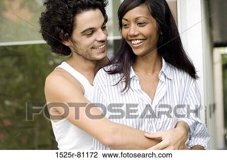 Stock Image - Close-up of a young man embracing a young woman from behind. Fotosearch