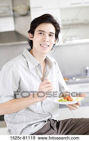Close-up of a young man holding a plate of salad and smiling View Large Photo Image Stock Photo - Close-up of a young man holding a plate of salad and smiling. Fotosearch