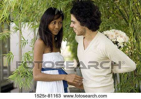 Close-up of a young man standing with a young woman and hiding a bouquet of flowers behind his back View Large Photo Image Stock Image - Close-up of a young man standing with a young woman and hiding a bouquet of flowers behind his back. Fotosearch