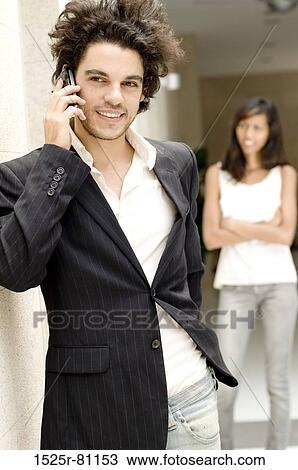 Close-up of a young man talking on a mobile phone with a young woman standing behind him View Large Photo Image Stock Image - Close-up of a young man talking on a mobile phone with a young woman standing behind him. Fotosearch