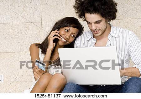 Close-up of a young man using a laptop with a young woman talking on a mobile phone beside him View Large Photo Image Stock Photo - Close-up of a young man using a laptop with a young woman talking on a mobile phone beside him. Fotosearch