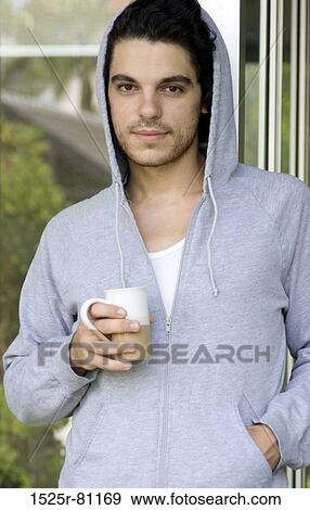 Close-up of a young man wearing a hooded shirt and holding a cup of tea View Large Photo Image Stock Photo - Close-up of a young man wearing a hooded shirt and holding a cup of tea. Fotosearch