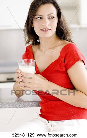 Close-up of a young woman sitting in a kitchen and holding a glass of milk View Large Photo Image Stock Photo - Close-up of a young woman sitting in a kitchen and holding a glass of milk. Fotosearch