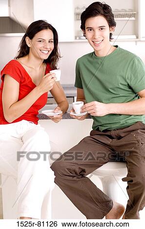 Portrait of a young couple sitting in a kitchen and holding cups of tea View Large Photo Image Stock Photograph - Portrait of a young couple sitting in a kitchen and holding cups of tea. Fotosearch