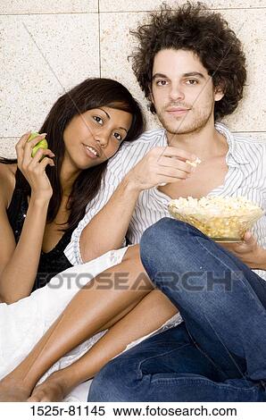 Stock Photography - Portrait of a young man sitting with a young woman holding a bowl of popcorn. Fotosearch