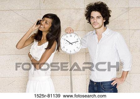 Portrait of a young man standing near a clock with a young woman talking on a mobile phone View Large Photo Image Stock Photo - Portrait of a young man standing near a clock with a young woman talking on a mobile phone. Fotosearch