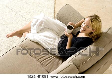 Portrait of a young woman sitting on a couch and holding a cup of black coffee View Large Photo Image Stock Image - Portrait of a young woman sitting on a couch and holding a cup of black coffee. Fotosearch