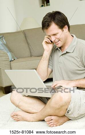 Side profile of a young man using a laptop and talking on a mobile phone View Large Photo Image Picture - Side profile of a young man using a laptop and talking on a mobile phone. Fotosearch