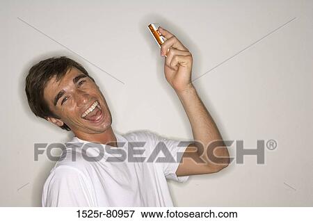 Portrait of a young man holding a mobile phone and laughing View Large Photo Image Stock Photo - Portrait of a young man holding a mobile phone and laughing. Fotosearch