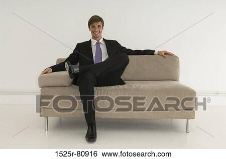 Stock Photograph - Portrait of a young man sitting on a couch and smiling. Fotosearch