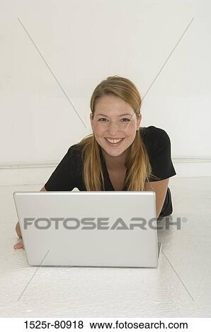 Portrait of a young woman lying on the floor in front of a laptop and smiling View Large Photo Image Stock Photo - Portrait of a young woman lying on the floor in front of a laptop and smiling. Fotosearch