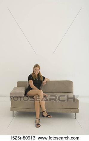 Portrait of a young woman sitting on a couch and smiling View Large Photo Image Stock Image - Portrait of a young woman sitting on a couch and smiling. Fotosearch
