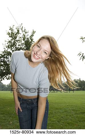 Picture - Portrait of a young woman standing in a park and smiling. Fotosearch