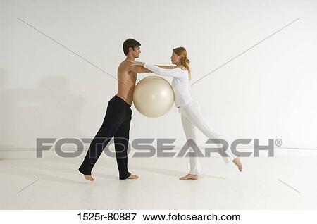 Stock Photo - Side profile of a young couple exercising with a fitness ball. Fotosearch