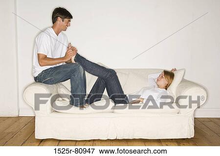 Side profile of a young woman lying on a couch and a young man holding her foot View Large Photo Image Stock Photo - Side profile of a young woman lying on a couch and a young man holding her foot. Fotosearch