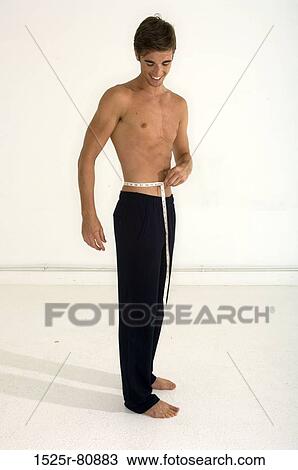 Young man measuring his waist with a tape measure and smiling View Large Photo Image Stock Image - Young man measuring his waist with a tape measure and smiling. Fotosearch