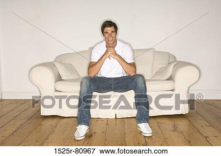 Young man sitting on a couch and smiling View Large Photo Image Stock Photo - Young man sitting on a couch and smiling. Fotosearch