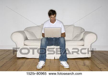 Stock Photography - Young man sitting on a couch and using a laptop. Fotosearch