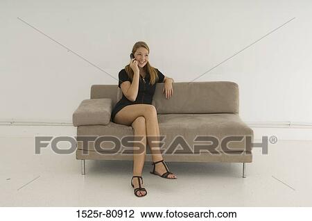 Young woman sitting on a couch and using a mobile phone View Large Photo Image Stock Image - Young woman sitting on a couch and using a mobile phone. Fotosearch