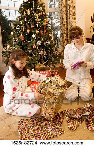 Picture - Girl and a teenage girl opening Christmas presents. Fotosearch